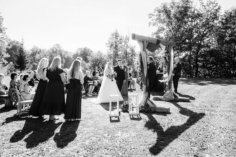 Svatební obřad pod otevřeným nebem, hosté sledují nevěstu a ženicha